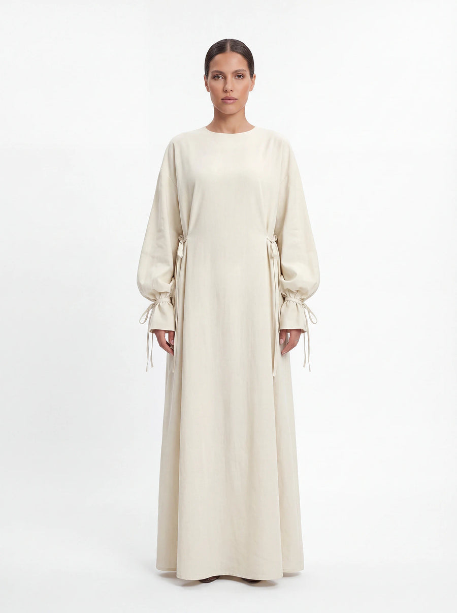Cremeweiße Abaya mit Schleifendetails an der Taille und den Ärmelabschlüssen, Frontalansicht.