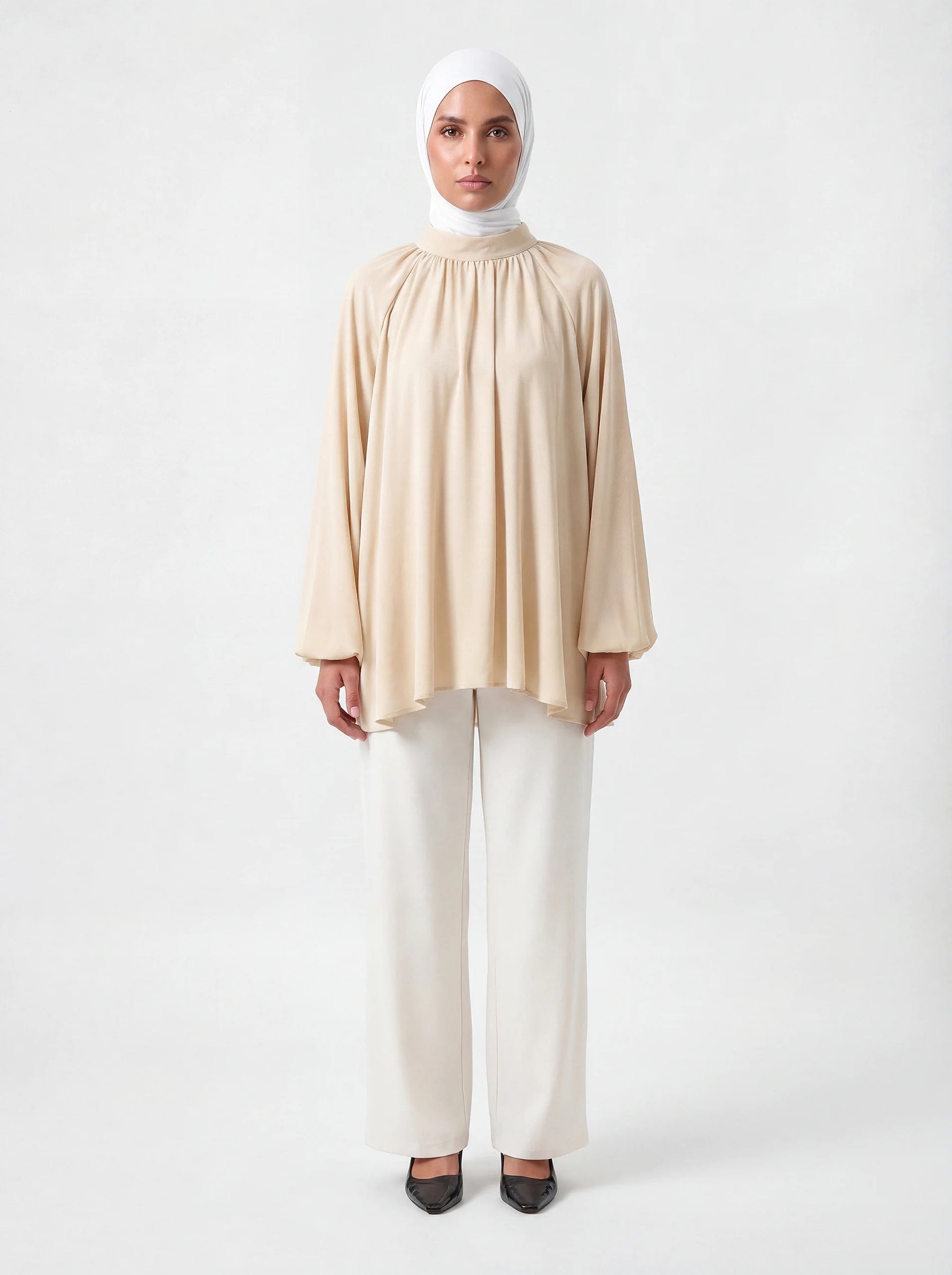 Beige Bluse mit Stehkragen, weiten Ballonärmeln und asymmetrischem Saum, Frontalansicht.