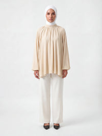 Beige Bluse mit Stehkragen, weiten Ballonärmeln und asymmetrischem Saum, Frontalansicht.