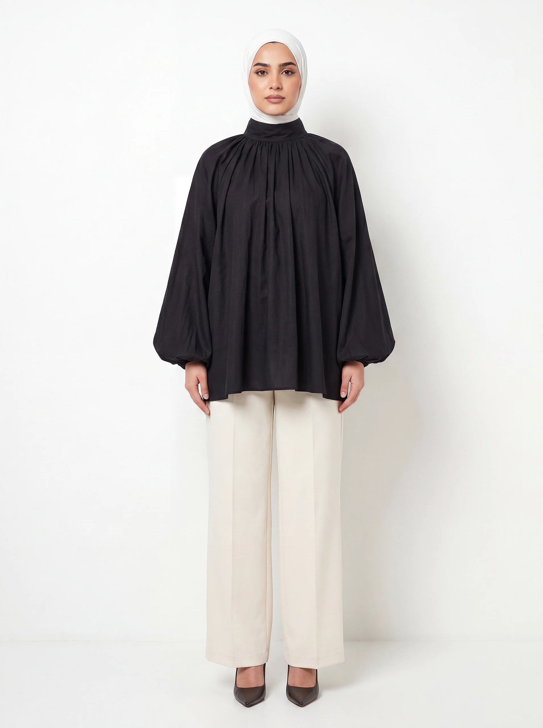 Schwarze Bluse mit Stehkragen, gerafften Ballonärmeln und weitem A-Linien-Schnitt, Frontalansicht.