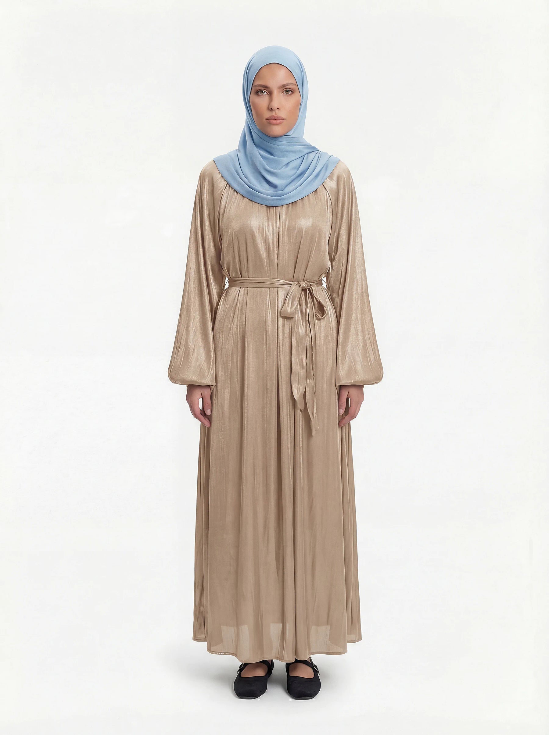Champagnerfarbene Abaya aus glänzendem Stoff mit Ballonärmeln und Bindegürtel, Frontalansicht mit hellblauem Hijab.