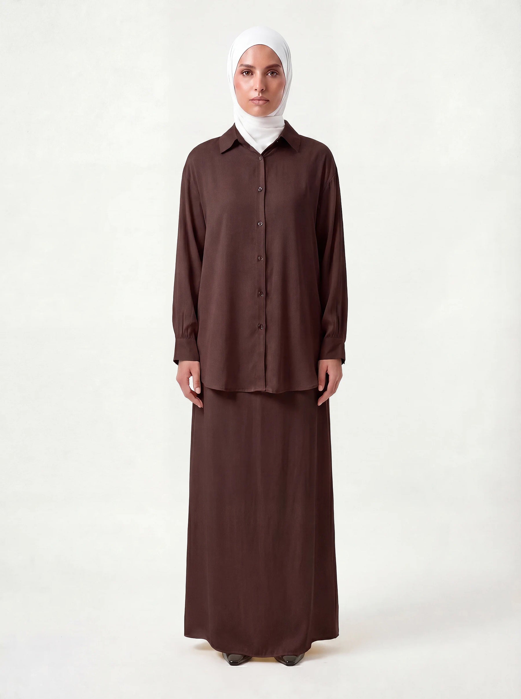 Schokobrauner Zweiteiler mit langärmeligem Hemd, Knopfleiste und bodenlangem Unterkleid, Frontalansicht.